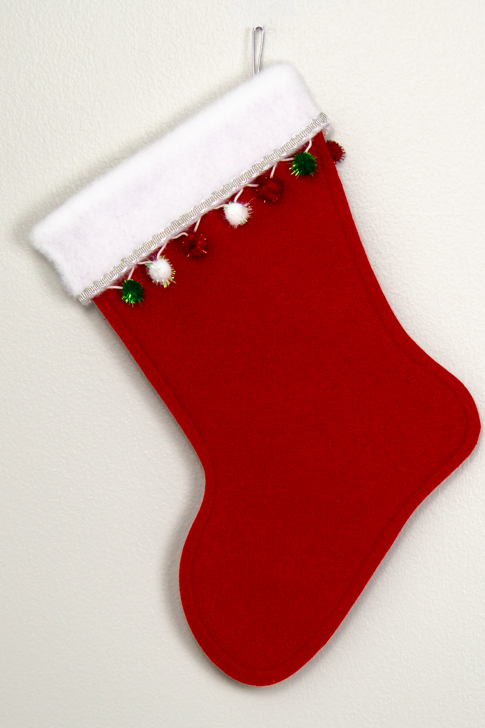 Holiday red felt handmade Christmas stocking with sparkly pom poms and decorated in white, green, red & silver. (back of Gingerbread stocking)