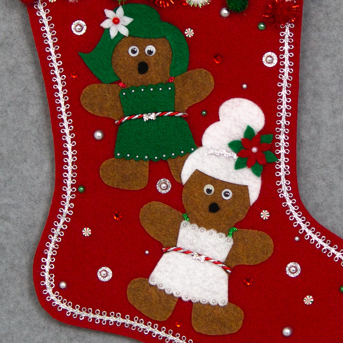 Twin copper felt Gingerbread on a holiday red felt handmade Christmas stocking with sparkly pom poms, felt poinsettias and decorated in white, green, red & silver. (front of stocking - close up detail of Gingerbread)
