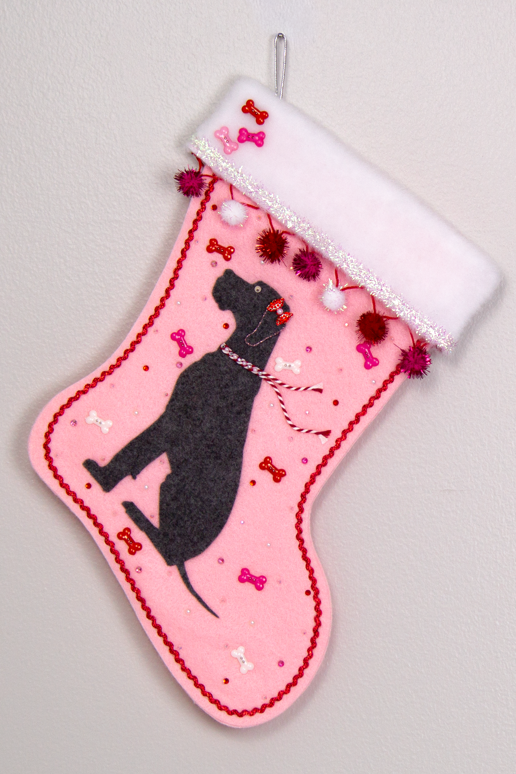 Charcoal gray Great Dane dog on light pink felt handmade Christmas stocking with sparkly pom poms, tinsel, bone buttons and decorated in red, pinks, white and silver. (front of stocking)