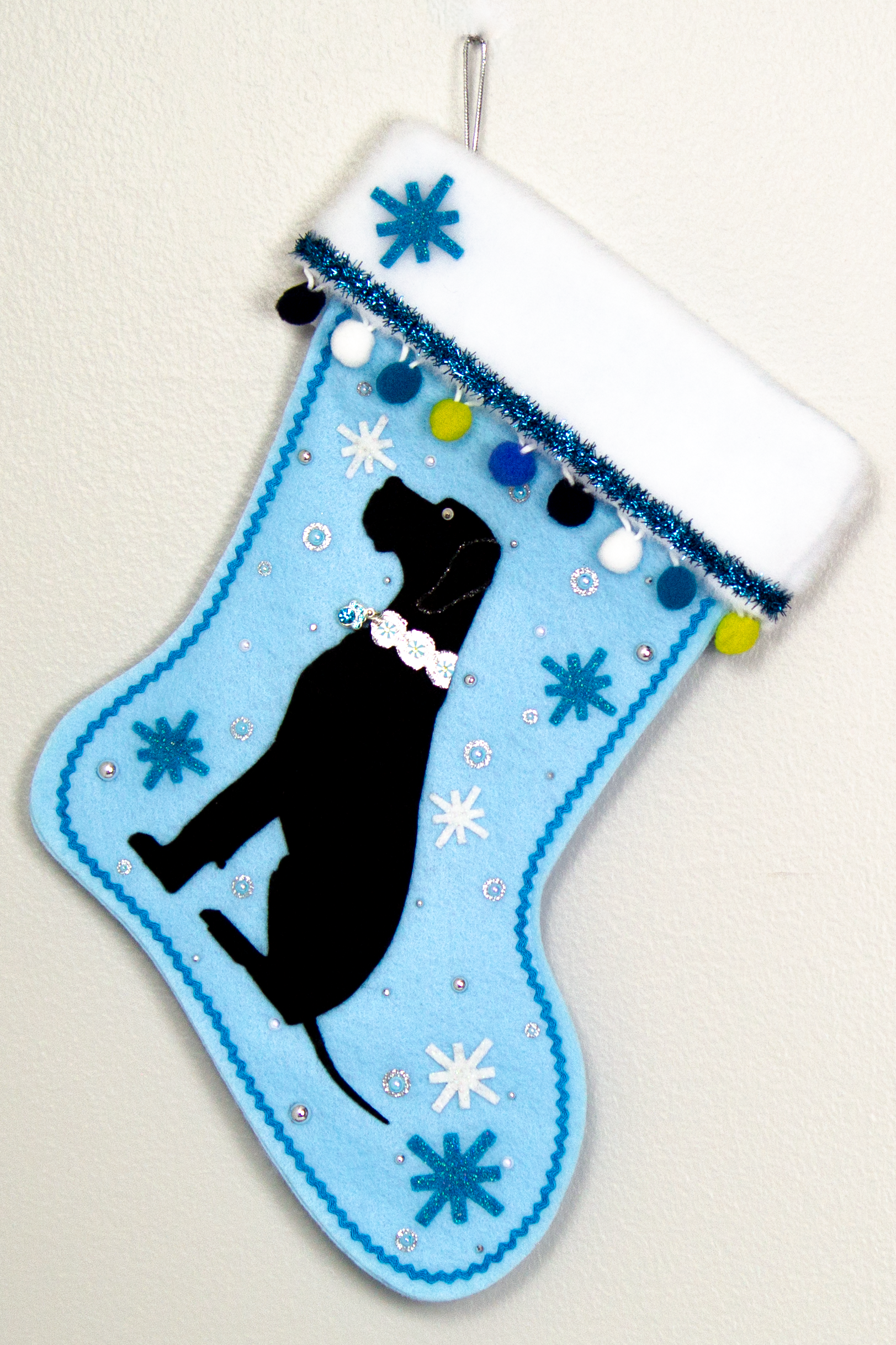 Black Great Dane dog on light blue felt handmade Christmas stocking with felt starbursts, pom poms, tinsel and decorated in white, blues, green and silver. (front of stocking)