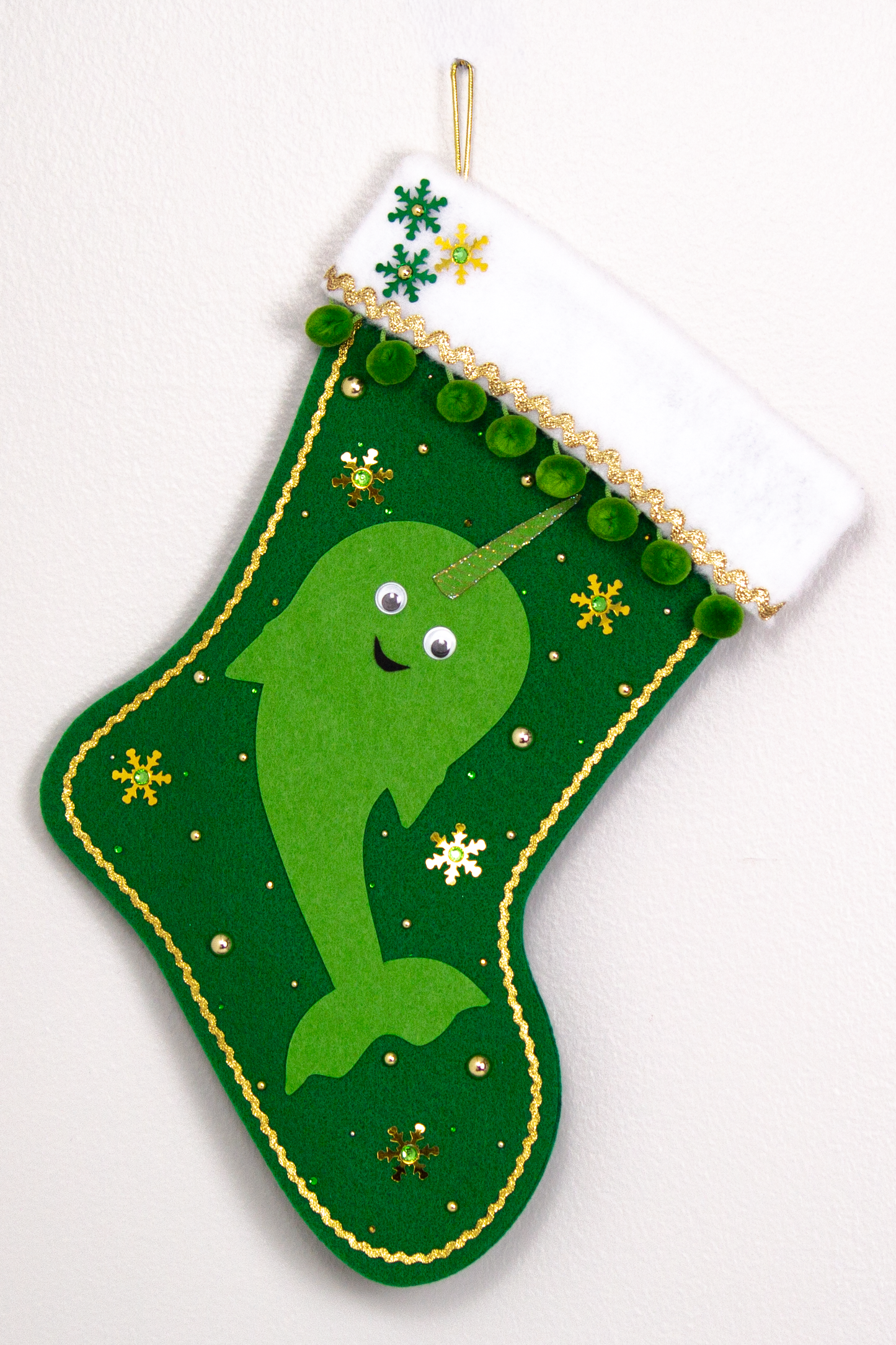 Bright green Narwhal on a holiday green felt handmade Christmas stocking with pom poms, googlie eyes, sequin snowflakes and decoration green & gold. (front of stocking)