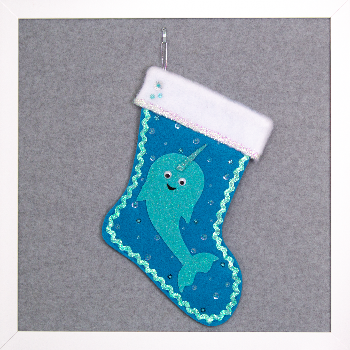 Glittery aqua Narwhal on a peacock blue felt handmade Christmas stocking with tinsel ribbon, googlie eyes and decoration in clear, aqua & silver. (front of stocking)