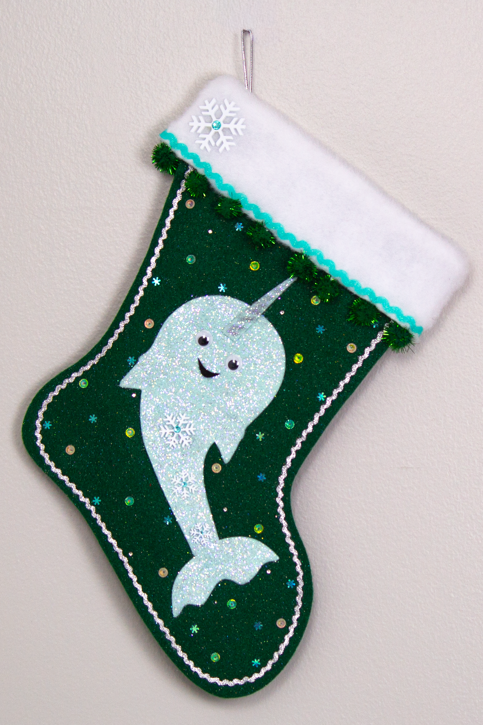 Mint green glittered Narwhal on dark green glitter felt handmade Christmas stocking with sparkly dark green pom poms, snowflake buttons and decorations in aqua, silver and multicolors. (front of stocking)