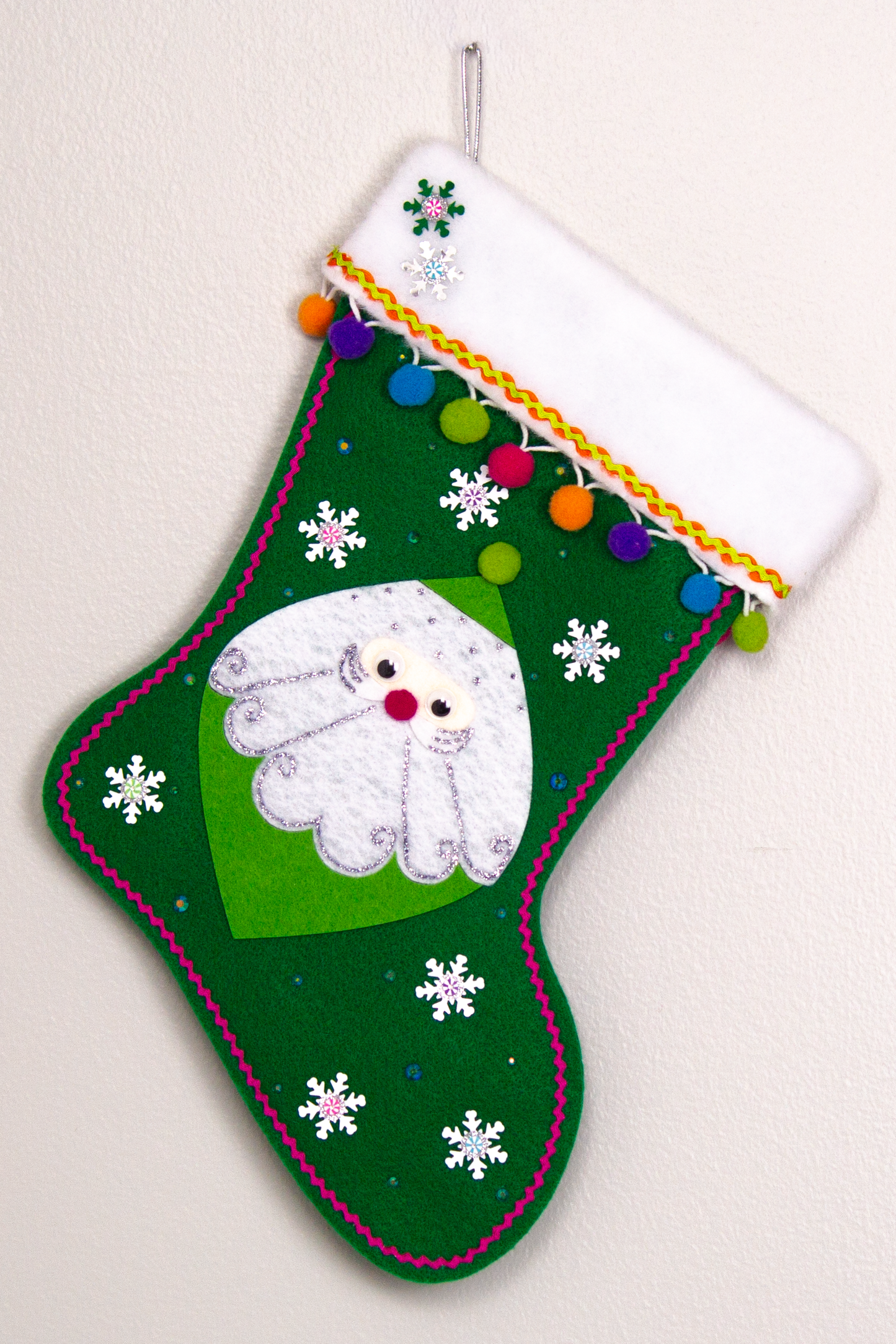Marquise shaped Santa in green on a holiday green felt handmade Christmas stocking with snowflake sequins, clay candy pieces, pom poms and decorated in orange, purple, blue, greens, hot pink & silver. (front of stocking)