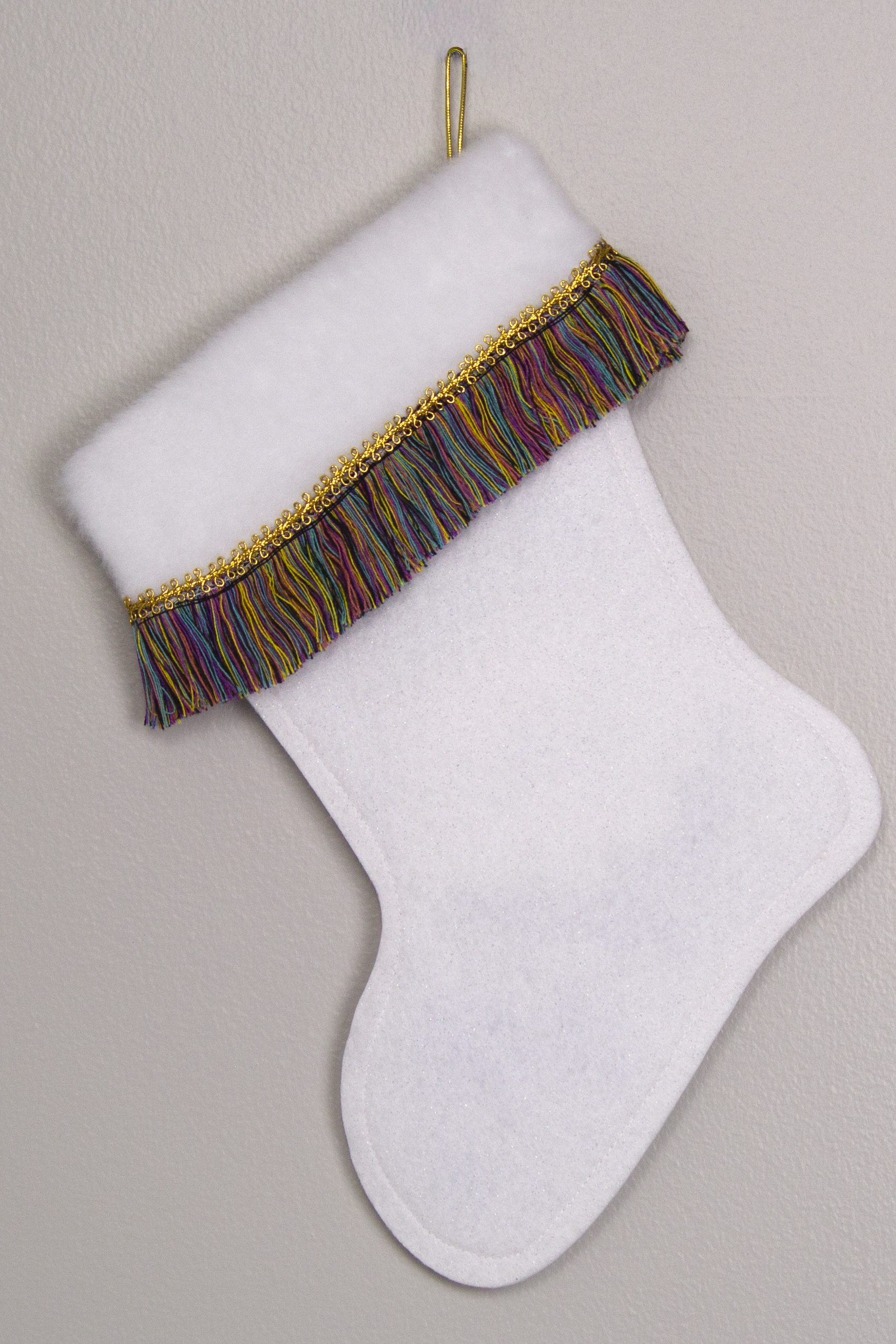 White glitter felt handmade Christmas stocking with multicolored fringe and decorated in gold. (back of marquise Santa stocking)