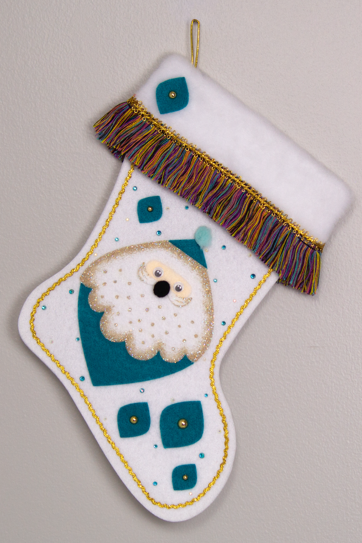 Marquise shaped Santa head (Holt Howard inspired) in turquoise with a gold glittered beard on a glitter white felt handmade Christmas stocking - felt marquise shapes, multicolored fringe  and decorated in turquoise & gold. (front of stocking)