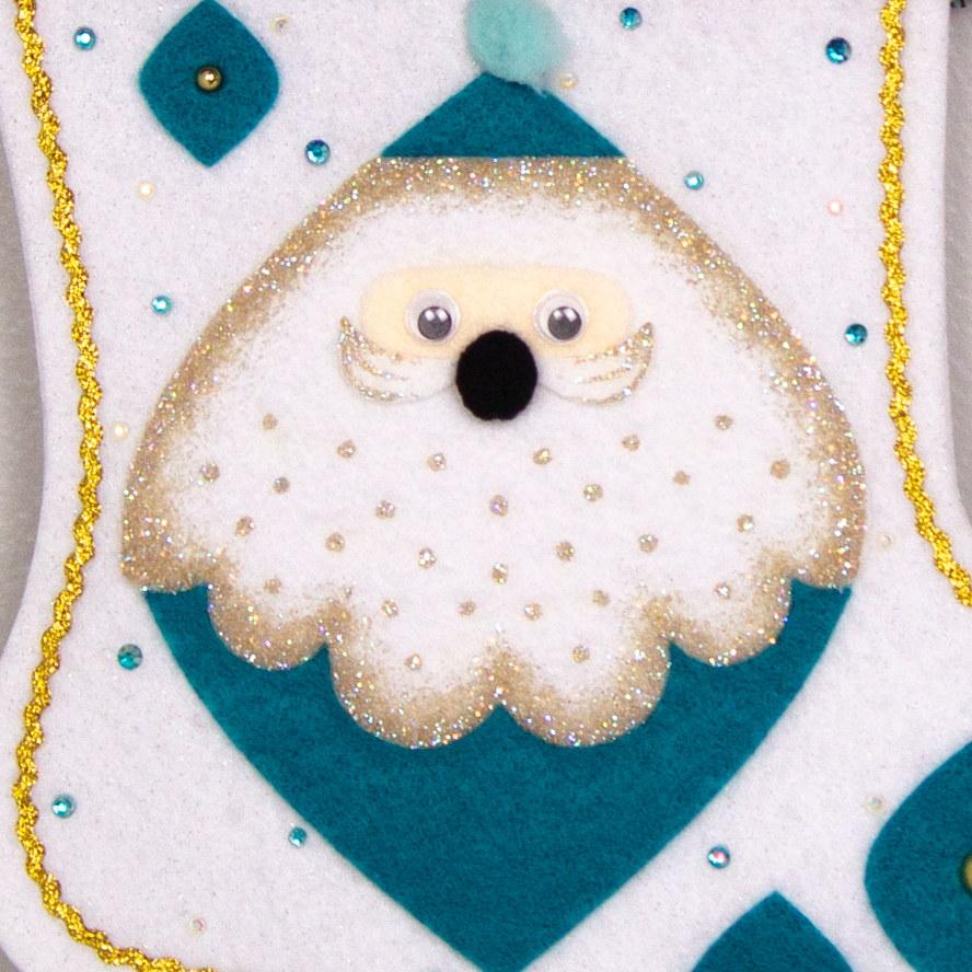 Marquise shaped Santa head (Holt Howard inspired) in turquoise with a gold glittered beard on a glitter white felt handmade Christmas stocking - felt marquise shapes, multicolored fringe  and decorated in turquoise & gold. (front of stocking - close up of painted details)