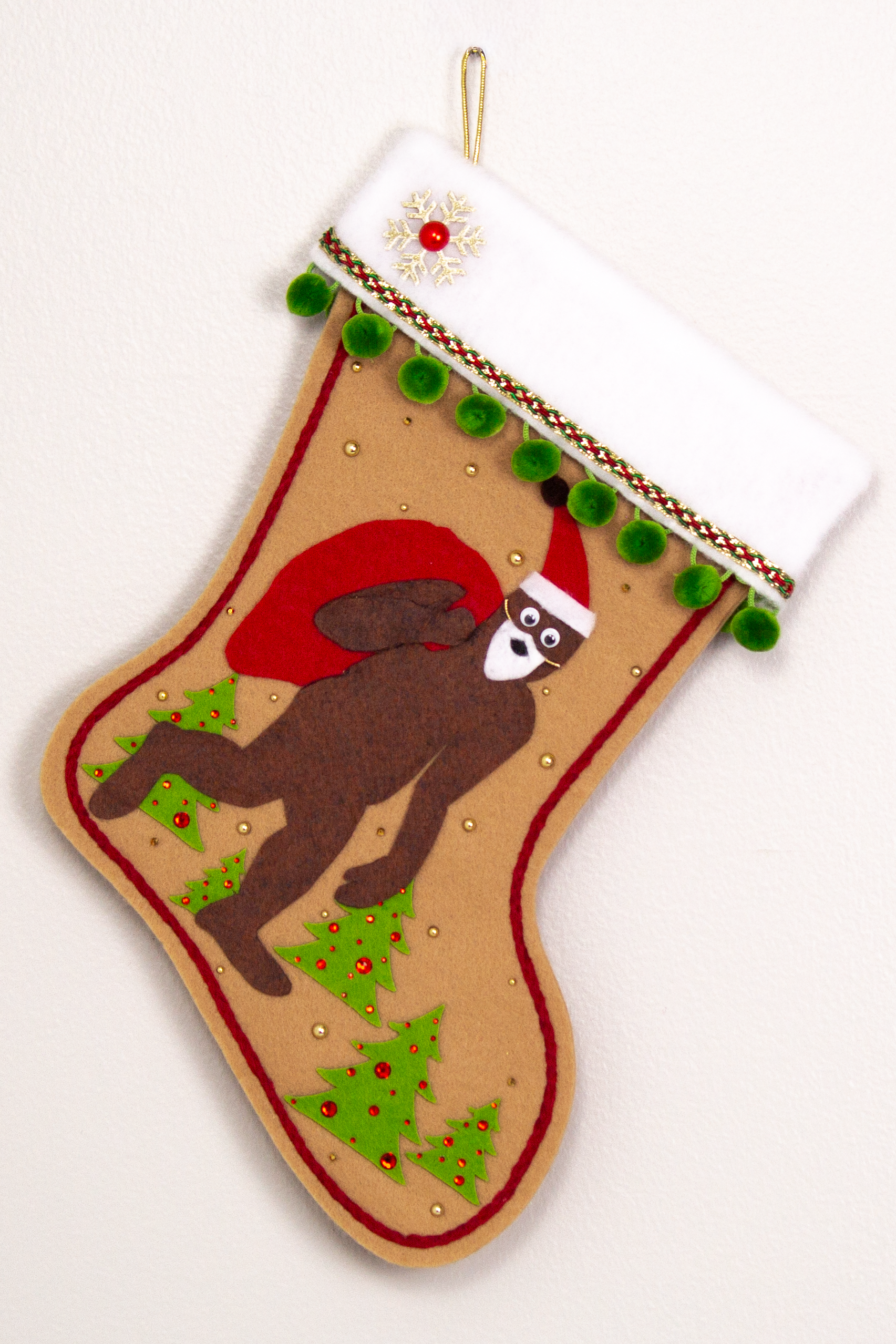 Felt Sasquatch Santa, red bag & hat on tan felt handmade Christmas stocking with pom poms, trees, a glittered snowflake button and decorated in green, red & gold. (front of stocking)