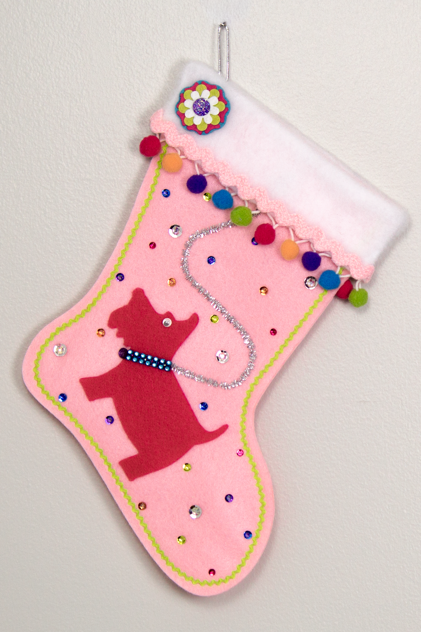 Bright pink Scottish Terrier Scottie dog on light pink felt handmade Christmas stocking with colorful pom poms and decorated in silver, pink, orange, purple, blue & green. (front of stocking)