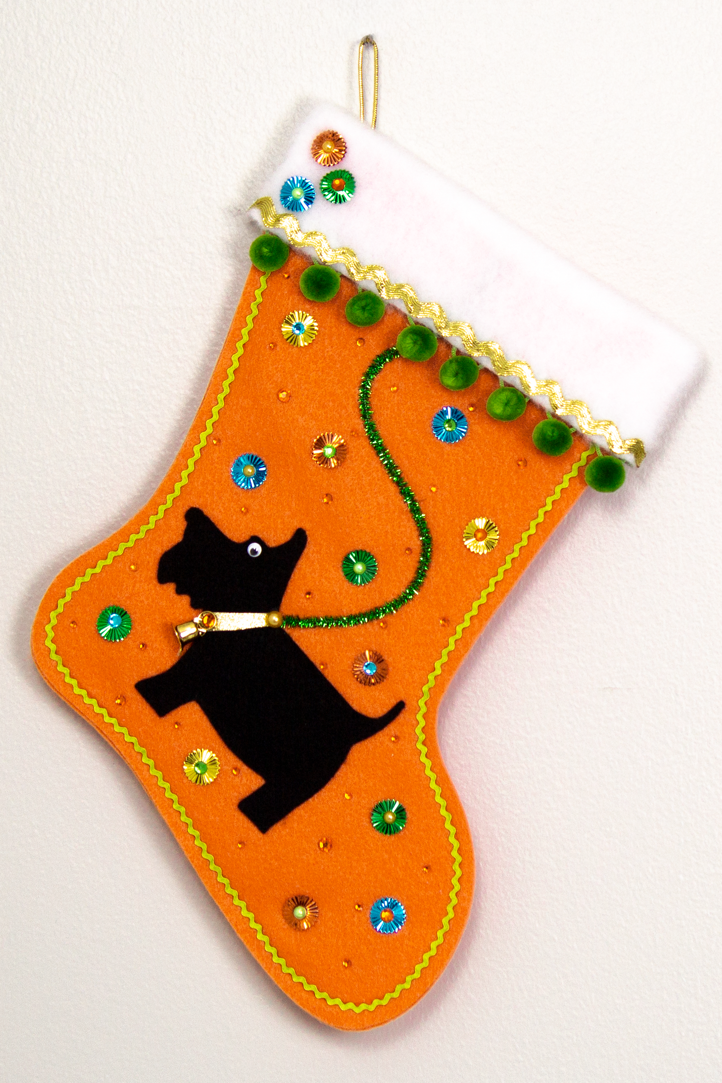 Black Scottish Terrier dog on orange felt handmade Christmas stocking with sunburst sequins, pom poms and decorated in gold, green, blue & orange. (front of stocking)