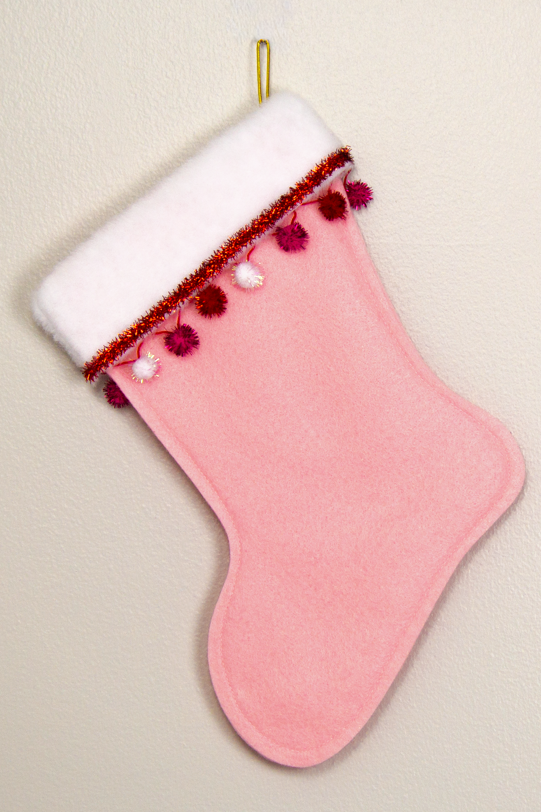 Light pink felt handmade Christmas stocking with sparkly pom poms, tinsel and decorated in red, pinks, white and gold. (back of Shih Tzu dog stocking)