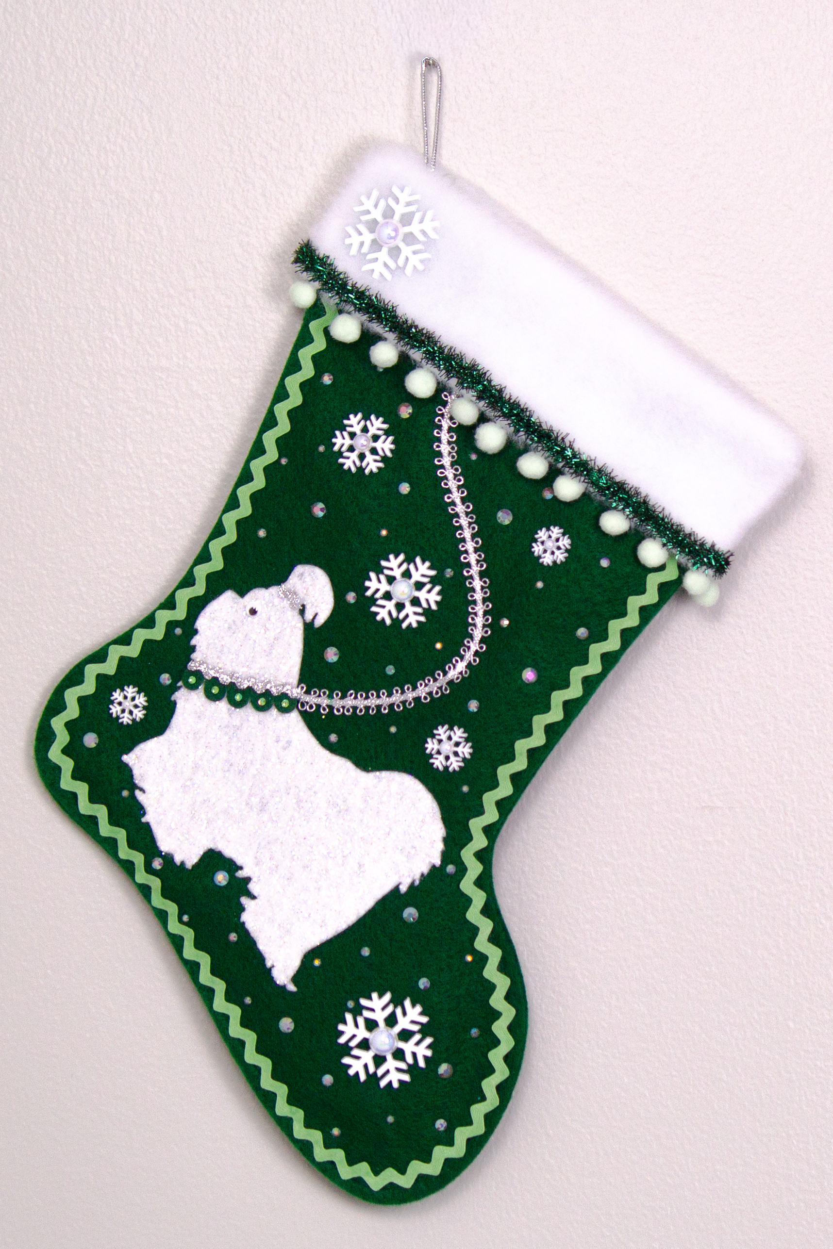 Glittered white Shih Tzu dog on dark green felt handmade Christmas stocking with pom poms, snowflake buttons, tinsel ribbon and decorations in white, mint green, silver, green and clear. (front of stocking)