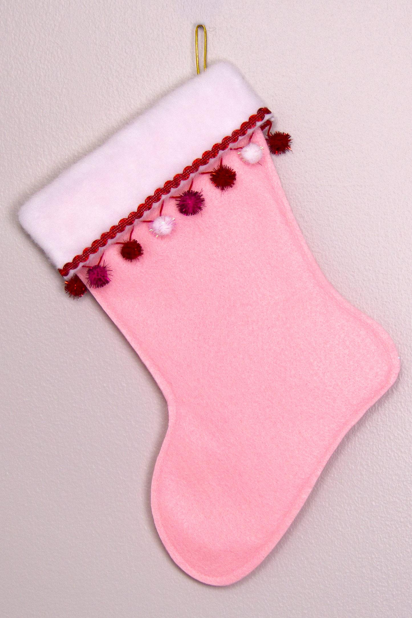 Light pink felt handmade Christmas stocking with sparkly pom poms and decoration in red, hot pink, white & gold. (back of T-Rex stocking)