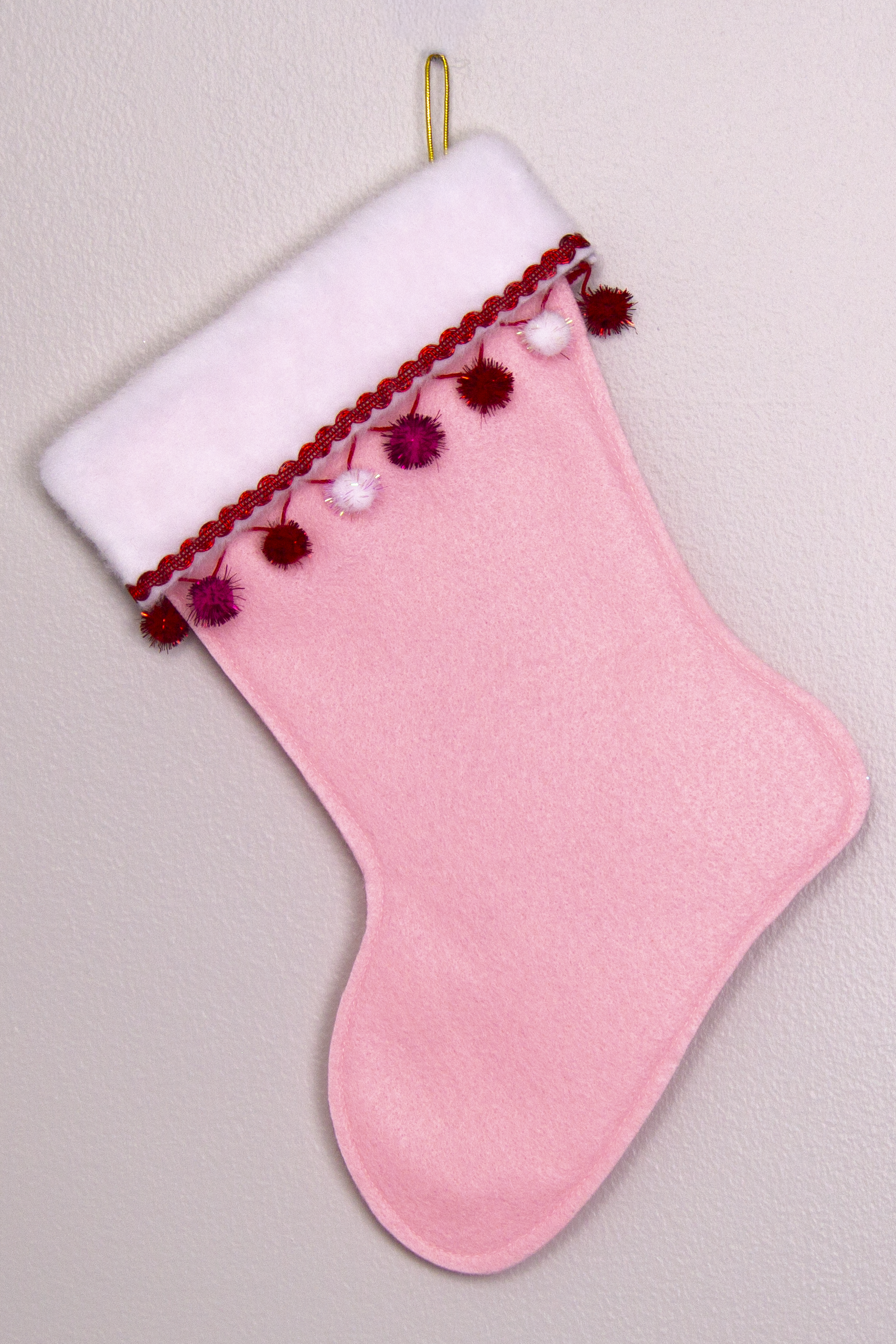 Light pink felt handmade Christmas stocking with sparkly pom poms and decoration in red, hot pink, white & gold. (back of T-Rex stocking)