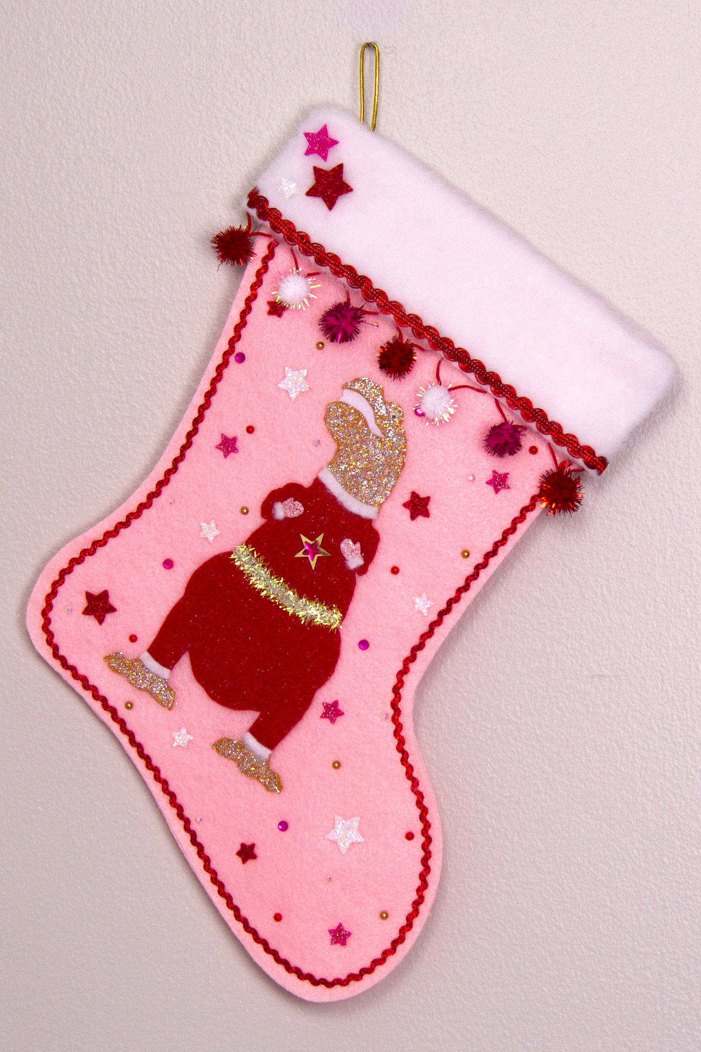 Gold glitter T-Rex with a red glitter felt suit on light pink felt handmade Christmas stocking with sparkly pom poms, felt glittery stars and decoration in red, hot pink, white & gold. (front of stocking)