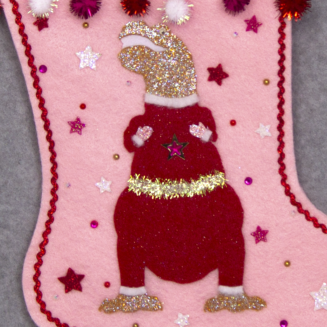 Gold glitter T-Rex with a red glitter felt suit on light pink felt handmade Christmas stocking with sparkly pom poms, felt glittery stars and decoration in red, hot pink, white & gold. (front of stocking - close up detail of T-Rex)