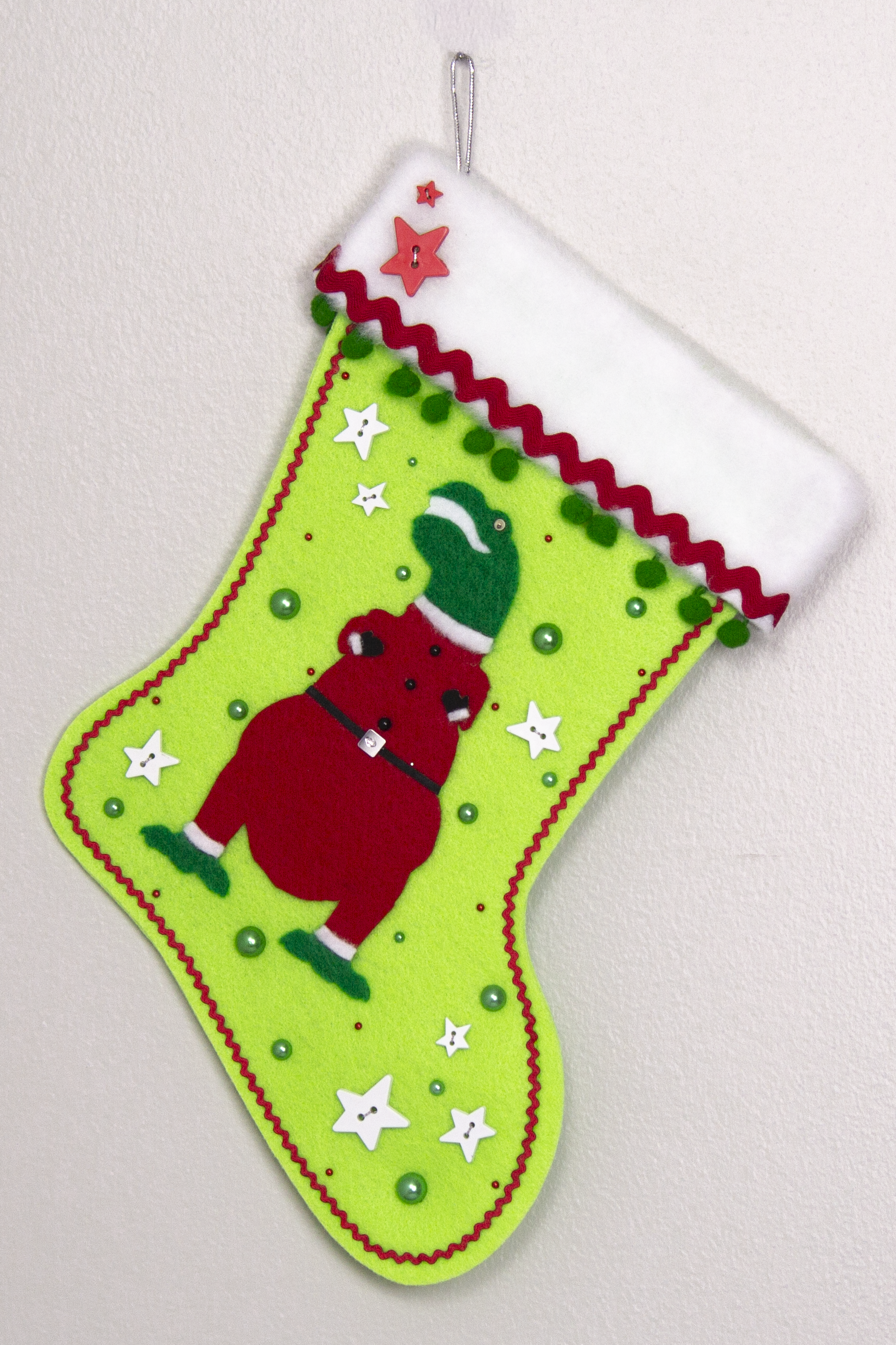 Holiday green T-Rex in a holiday red suit on neon green felt handmade Christmas stocking with pom poms, star buttons and decorations in red, green, white & silver. (front of stocking)