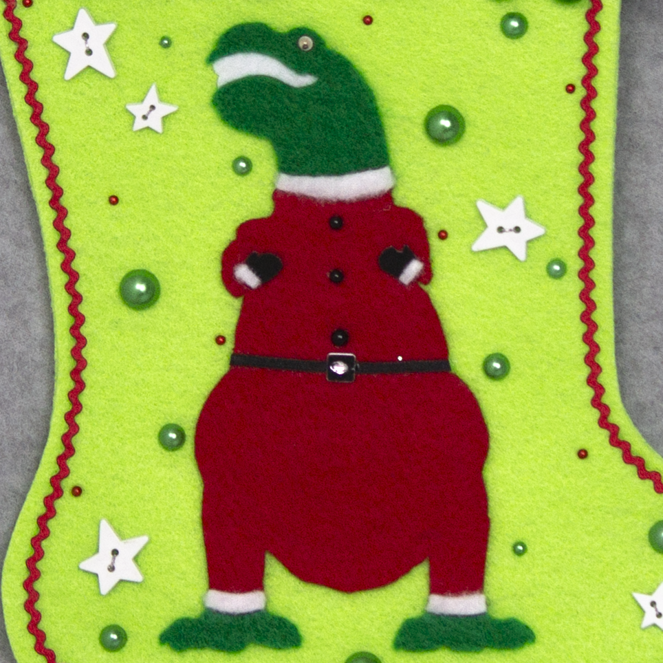 Holiday green T-Rex in a holiday red suit on neon green felt handmade Christmas stocking with pom poms, star buttons and decorations in red, green, white & silver. (front of stocking - close up detail of T-Rex)