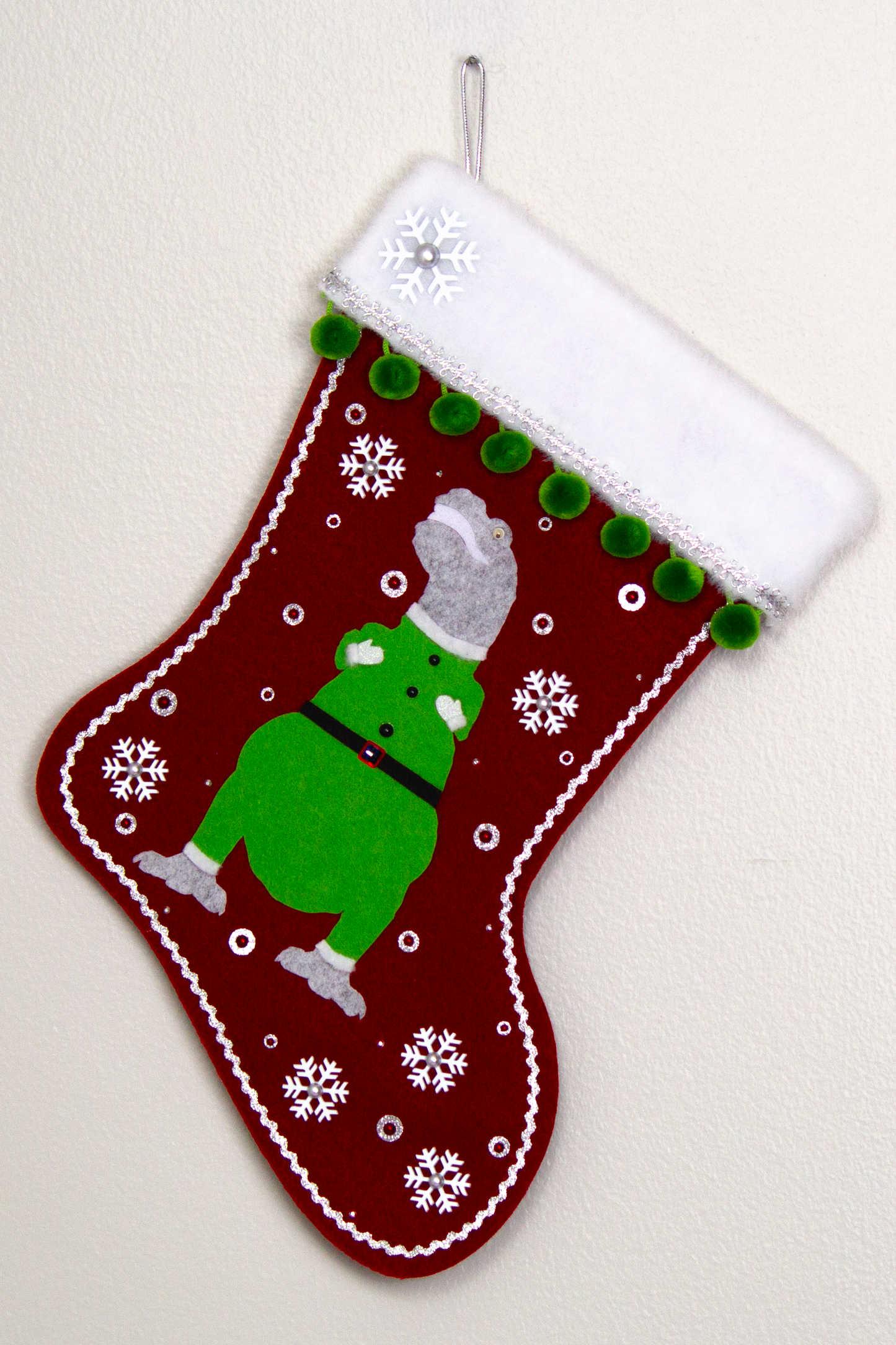 Variegated gray felt T-Rex with green suit on ruby red felt handmade Christmas stocking with pom poms,  snowflake buttons and decoration in white, ruby, green & silver. (front of stocking)