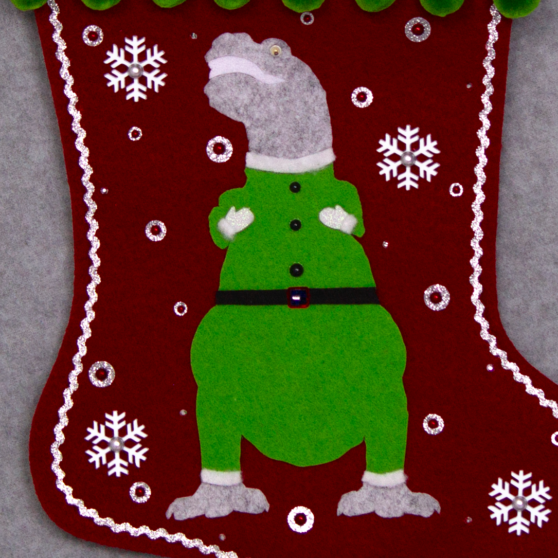 Variegated gray felt T-Rex with green suit on ruby red felt handmade Christmas stocking with pom poms,  snowflake buttons and decoration in white, ruby, green & silver. (front of stocking - close up detail of T-Rex)