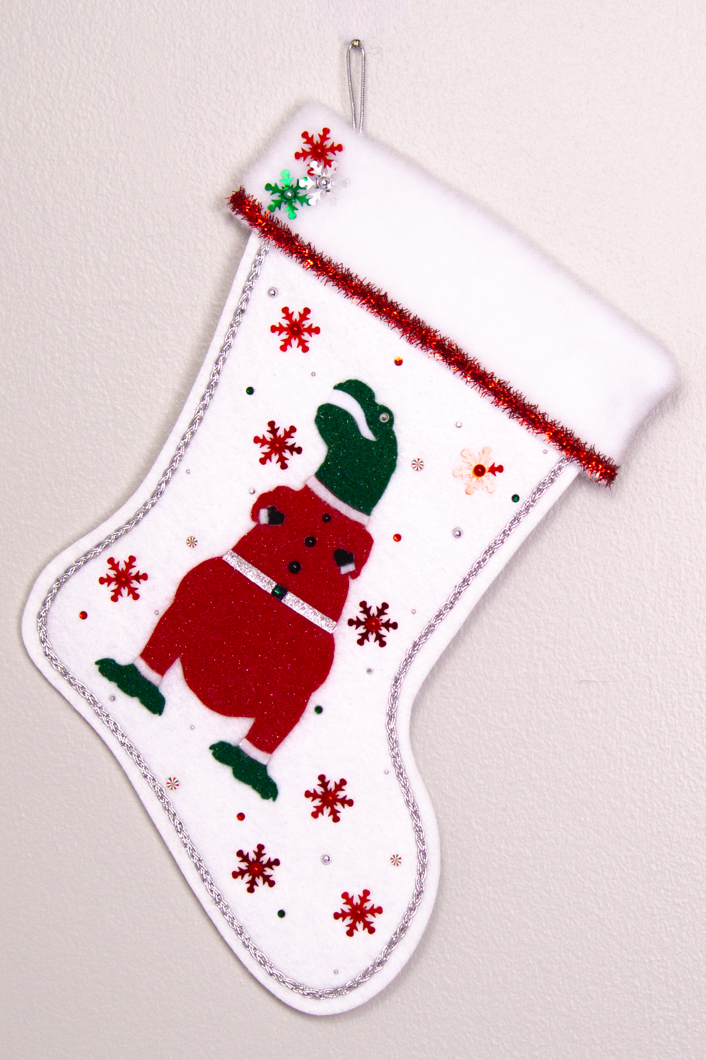 Dark green glitter felt T-Rex with red glitter suit on white glitter felt handmade Christmas stocking with tinsel ribbon, snowflake sequins and decoration in red, green & silver. (front of stocking)