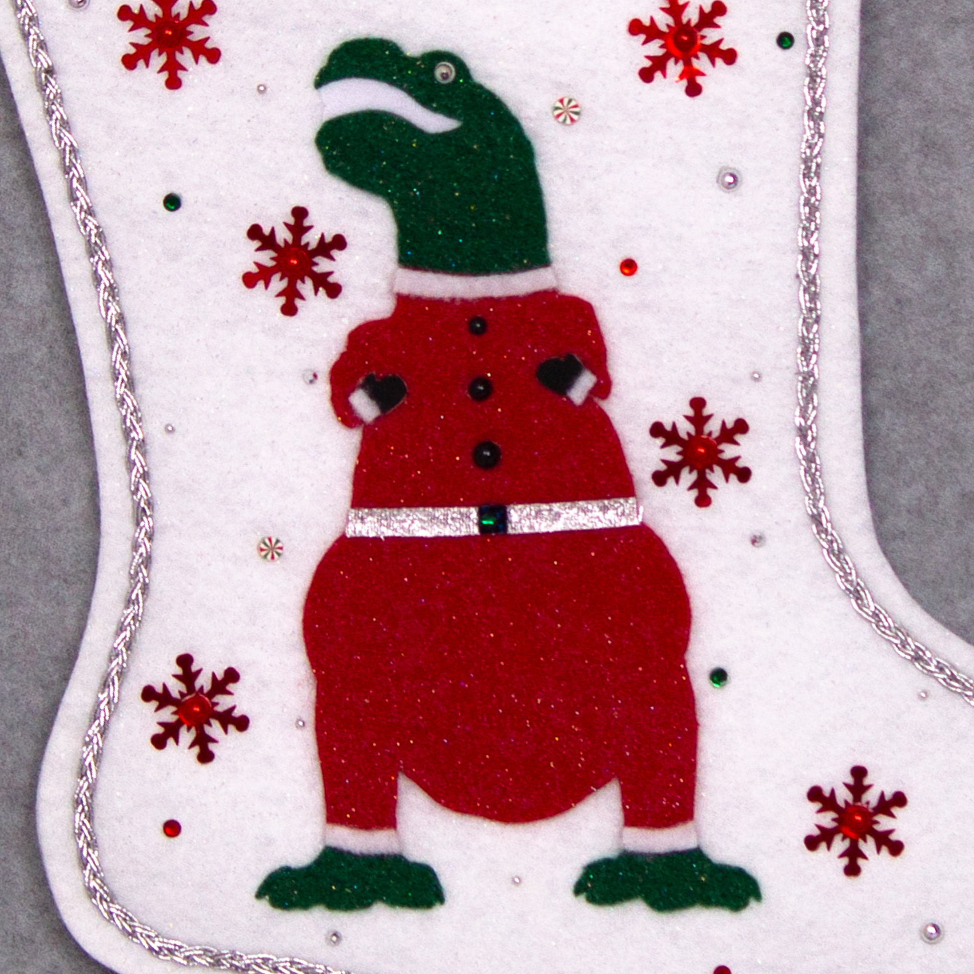 Dark green glitter felt T-Rex with red glitter suit on white glitter felt handmade Christmas stocking with tinsel ribbon, snowflake sequins and decoration in red, green & silver. (front of stocking - close up detail of T-Rex)