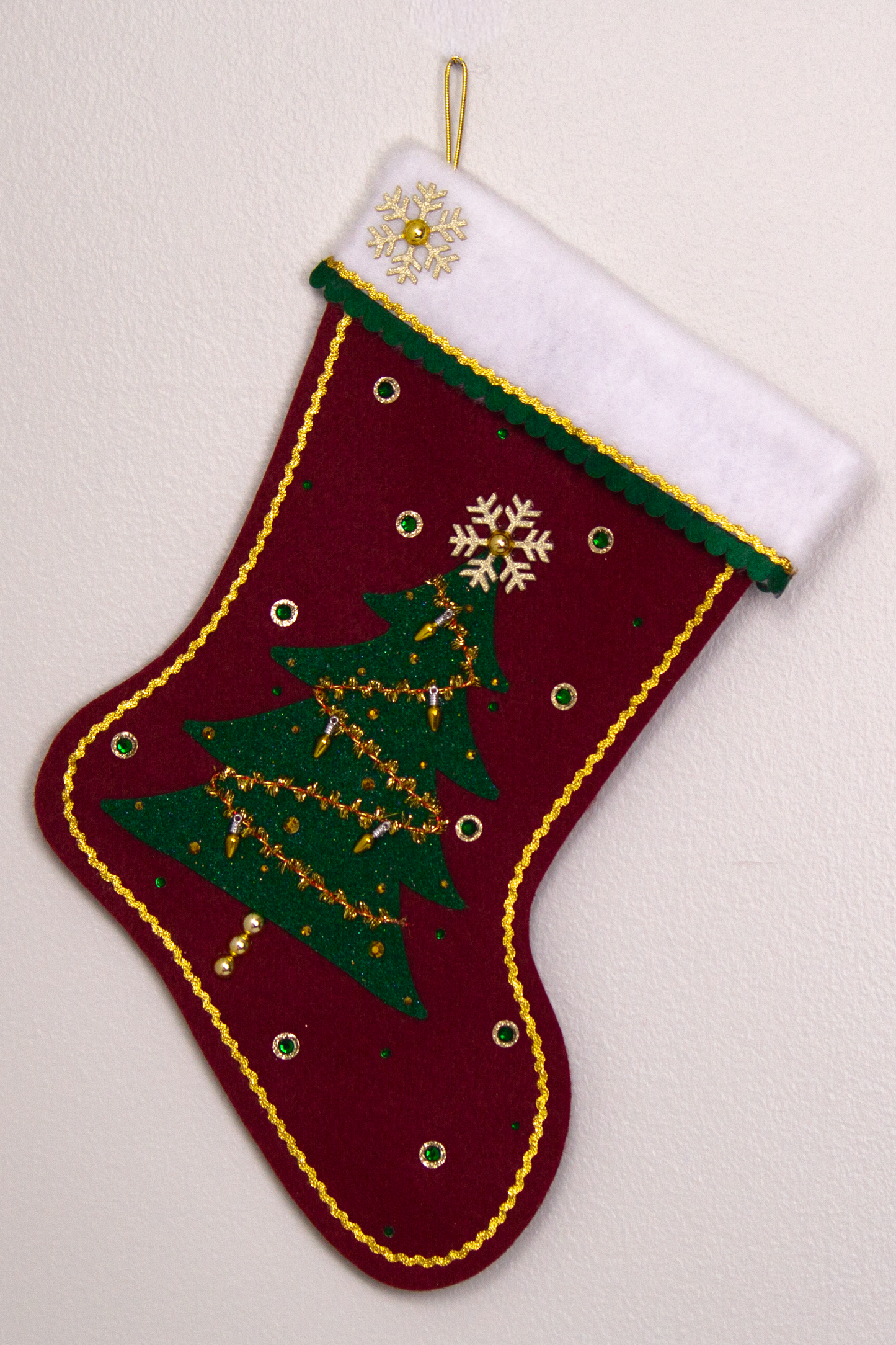 Dark green glitter Christmas Tree with tinsel, fake lights and topped with a gold glitter snowflake button on a ruby red felt handmade Christmas stocking, decorated in gold, green & red. (front of stocking)
