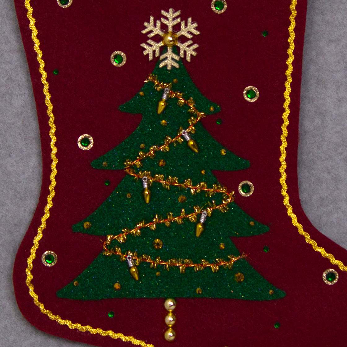 Dark green glitter Christmas Tree with tinsel, fake lights and topped with a gold glitter snowflake button on a ruby red felt handmade Christmas stocking, decorated in gold, green & red. (front of stocking - close up detail of tree)