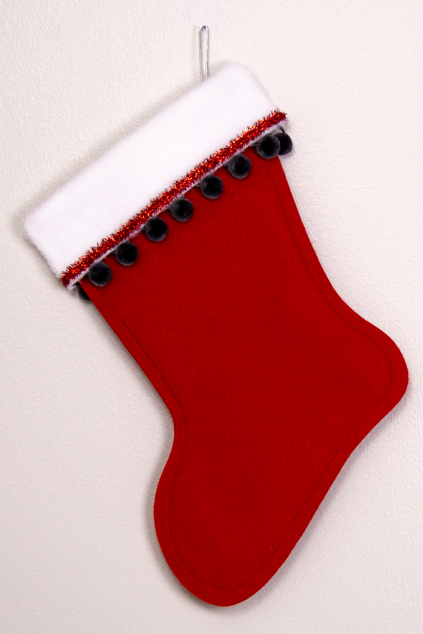 Holiday red felt handmade Christmas stocking with tinsel, pom poms and decorated in red, dark gray and silver.