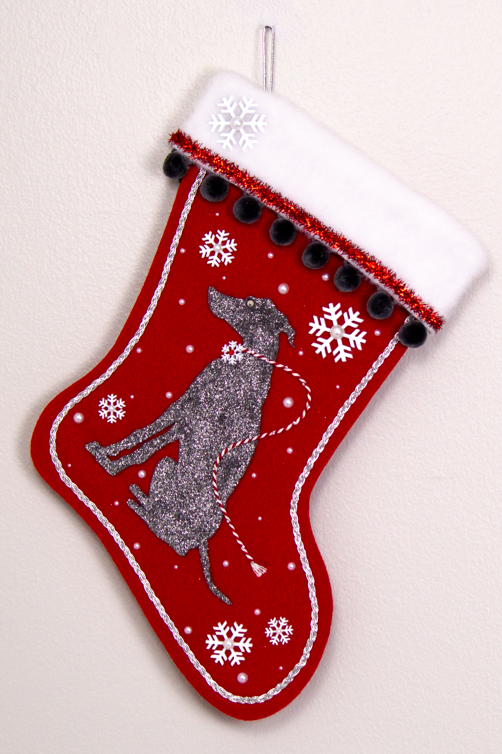 Silver glittered dark gray Whippet dog on a holiday red felt handmade Christmas stocking with snowflakes, tinsel, pom poms and decorated in red, white, dark gray and silver.