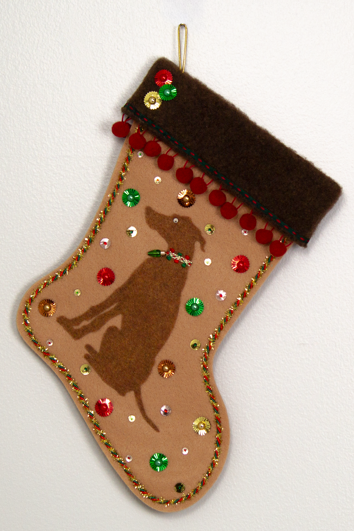 Copper Whippet dog on tan felt handmade Christmas stocking with pom poms, sunburst sequins and decorated in red, green, gold and copper. (front of stocking)