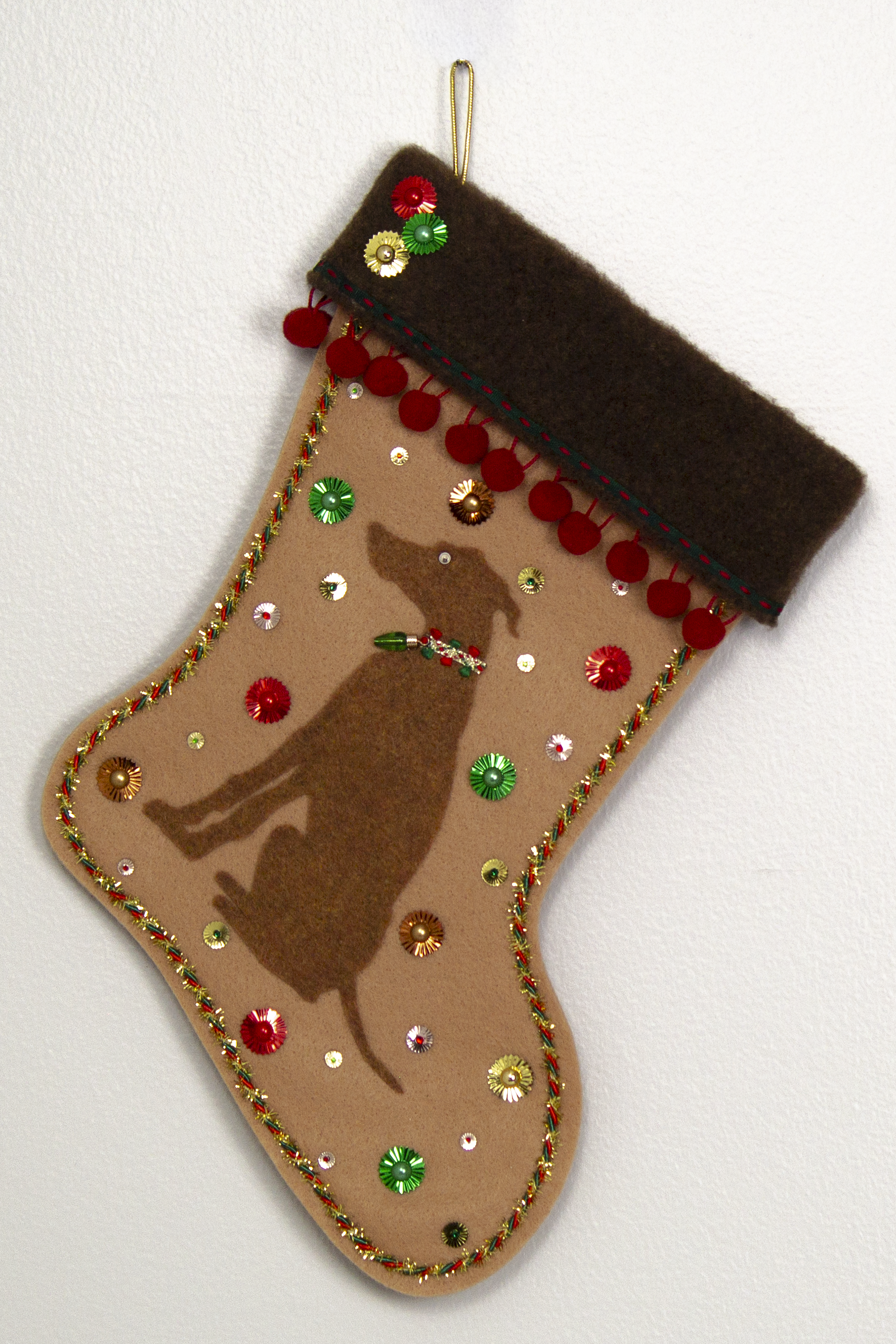 Copper Whippet dog on tan felt handmade Christmas stocking with pom poms, sunburst sequins and decorated in red, green, gold and copper. (front of stocking)