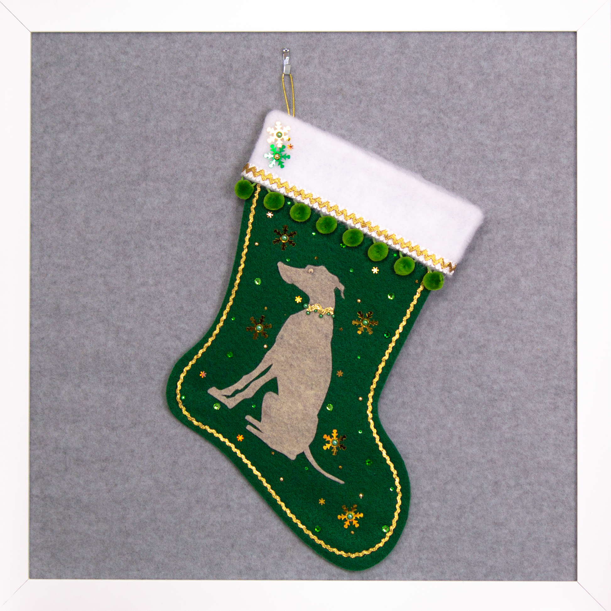 Sandstone beige Whippet dog on dark green felt handmade Christmas stocking with snowflake sequins, pom poms and decorated in gold and green. (front of stocking)